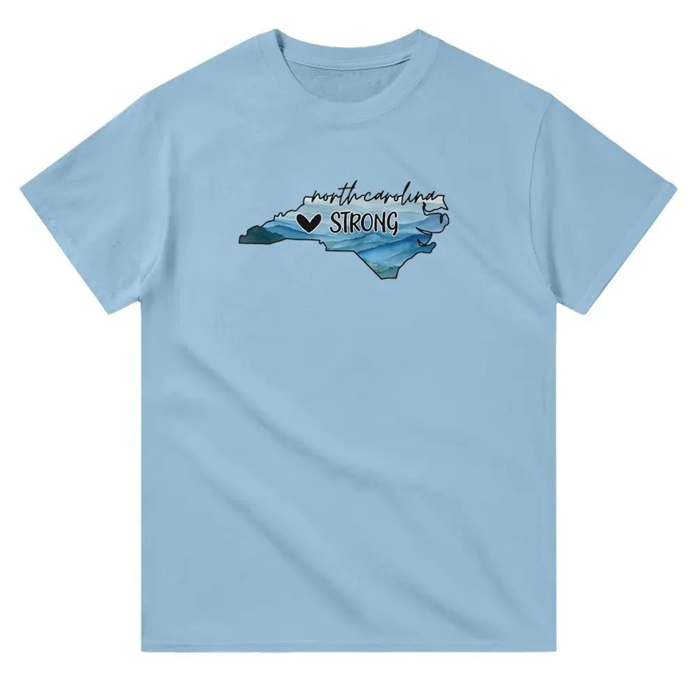 Blue T-shirt featuring an outline of North Carolina filled with blue and green tones, symbolizing a resilient landscape. Above the shape, the text reads "North Carolina" in a cursive font, with "STRONG" written below alongside a small heart icon. This design conveys a message of support and resilience, possibly for hurricane relief efforts.