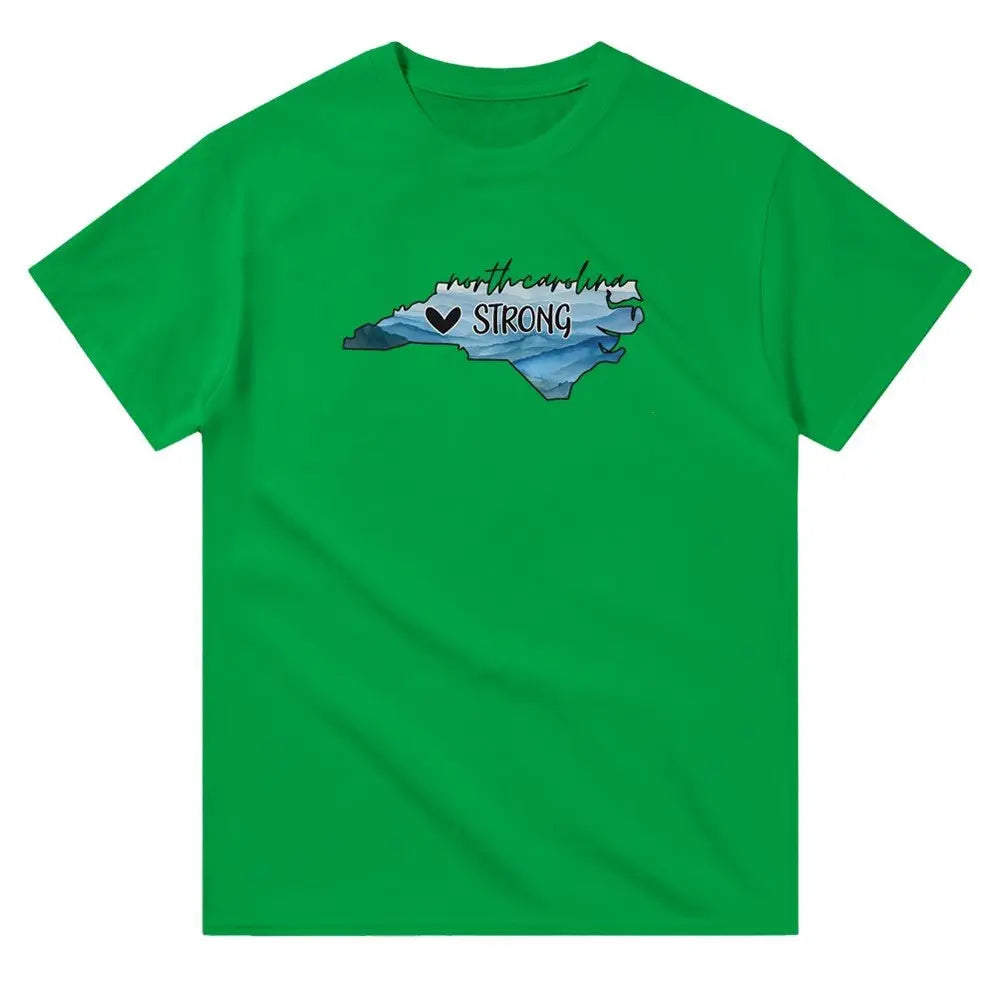 Green T-shirt featuring an outline of North Carolina filled with blue and green tones, symbolizing a resilient landscape. Above the shape, the text reads "North Carolina" in a cursive font, with "STRONG" written below alongside a small heart icon. This design conveys a message of support and resilience, possibly for hurricane relief efforts.