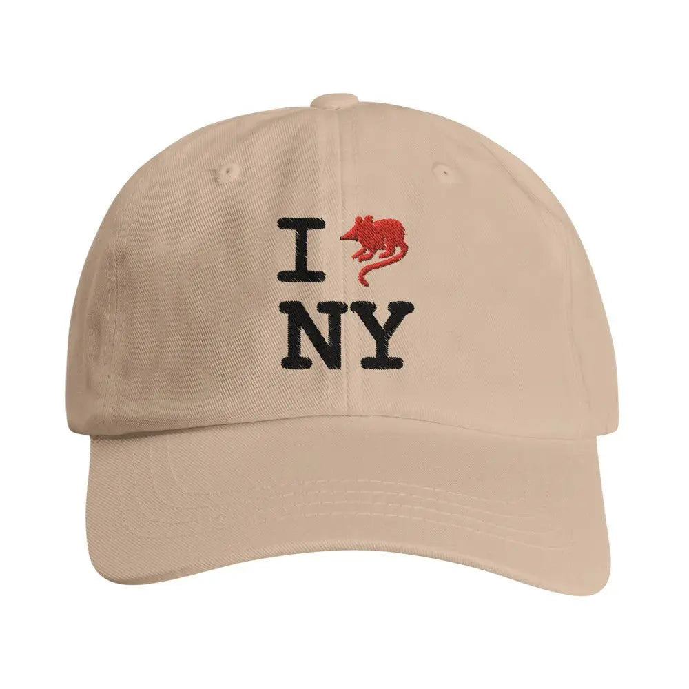 Beige baseball cap with an embroidered design reading "I [rat graphic] NY." The iconic heart symbol is replaced with a red rat, giving a gritty, humorous twist to the classic "I heart NY" logo, reflecting New York City's urban charm and character.