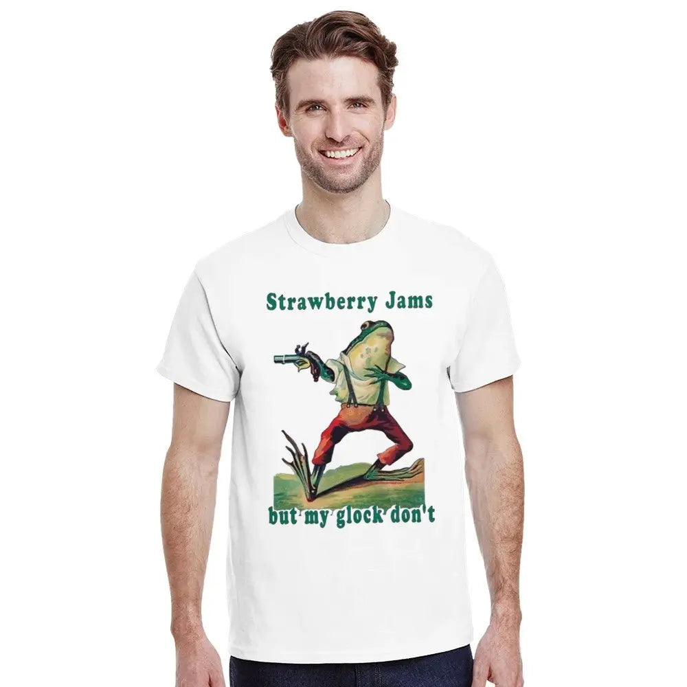 White T-shirt featuring a humorous illustration of a frog dressed in vintage-style clothing, holding a gun. Above the frog, the text reads, "Strawberry Jams, but my glock don't," in a playful, retro font. The design combines whimsical art with a tongue-in-cheek message.