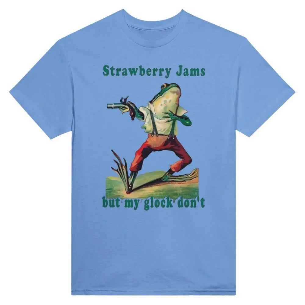 Blue T-shirt featuring a humorous illustration of a frog dressed in vintage-style clothing, holding a gun. Above the frog, the text reads, "Strawberry Jams," and below it says, "but my glock don't," in a playful, retro font. The design combines whimsical art with a tongue-in-cheek message.