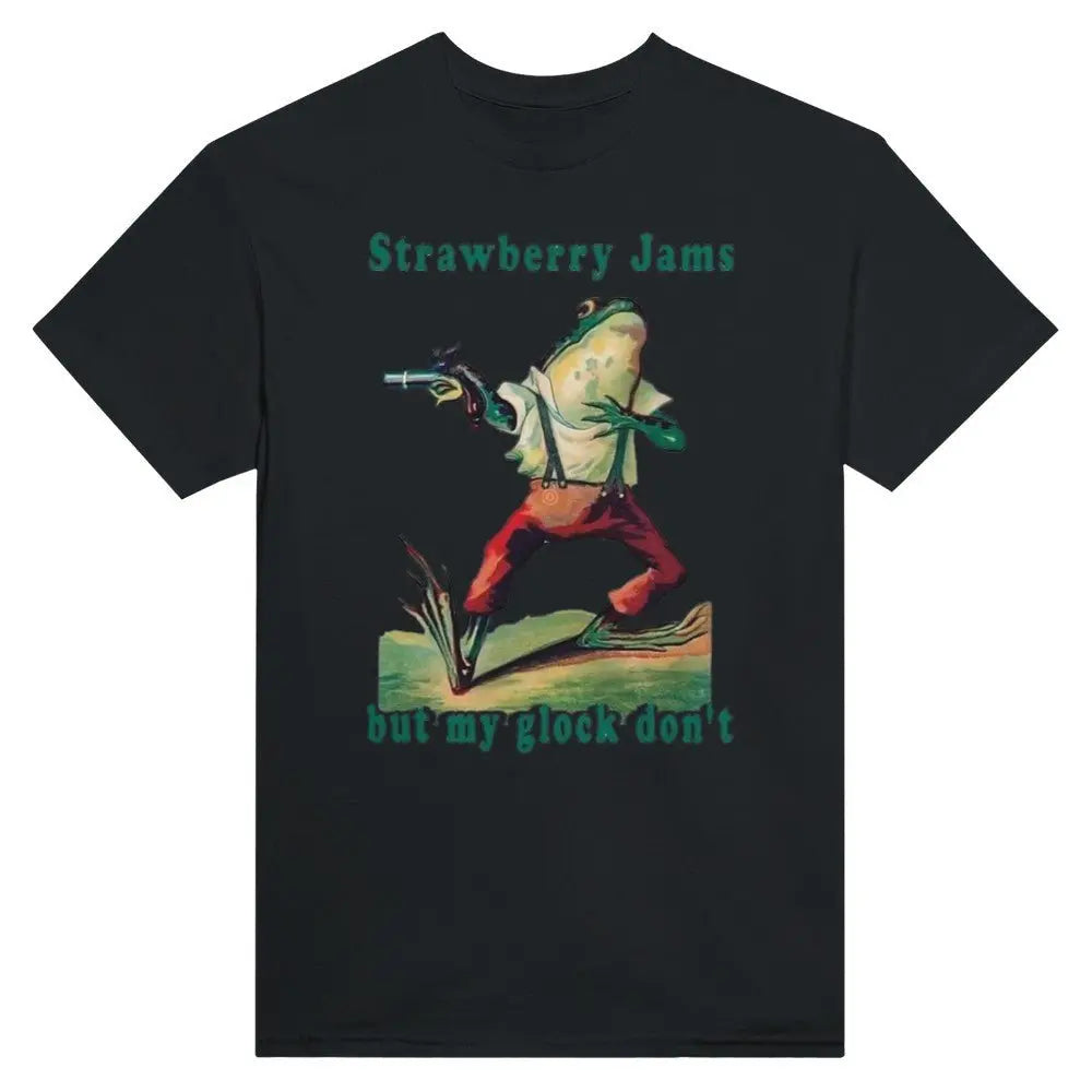 Black T-shirt featuring a humorous illustration of a frog dressed in vintage-style clothing, holding a gun. Above the frog, the text reads, "Strawberry Jams, but my glock don't," in a playful, retro font. The design combines whimsical art with a tongue-in-cheek message.